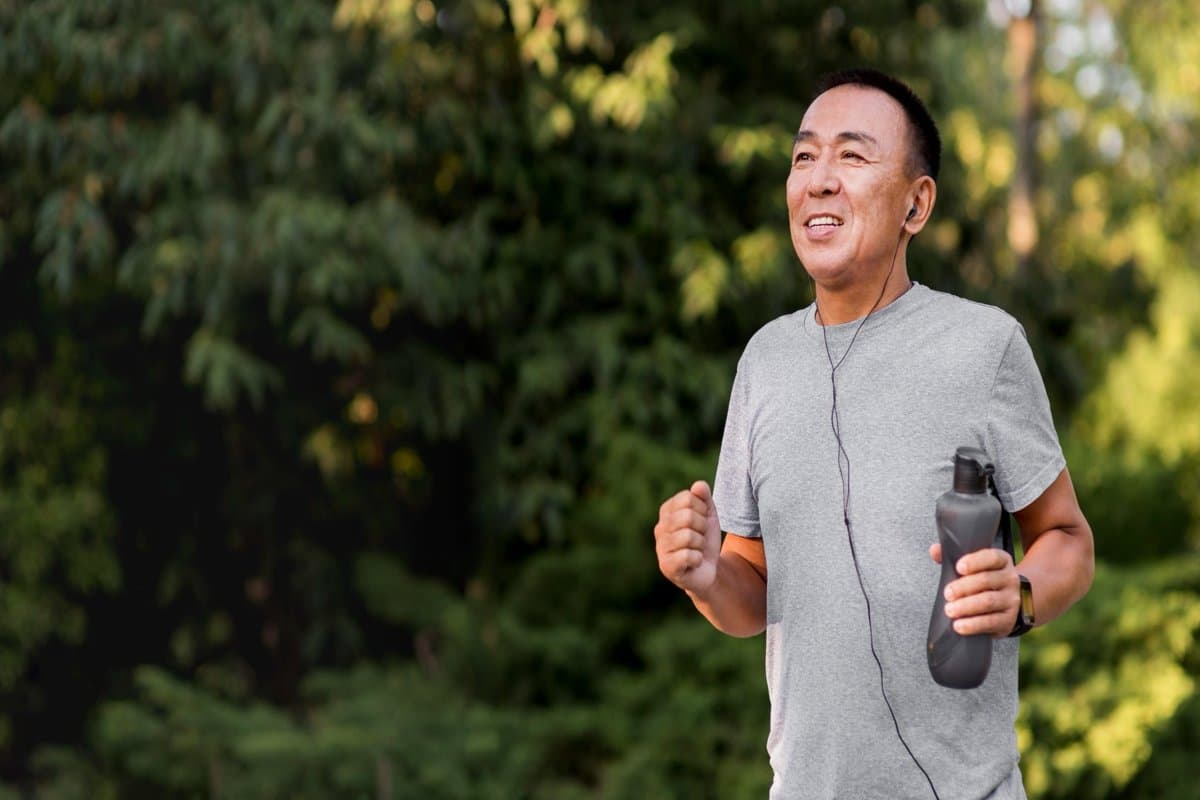 Pria paruh baya berolahraga lari di taman dengan earphone dan botol minum, mencerminkan gaya hidup aktif dan sehat